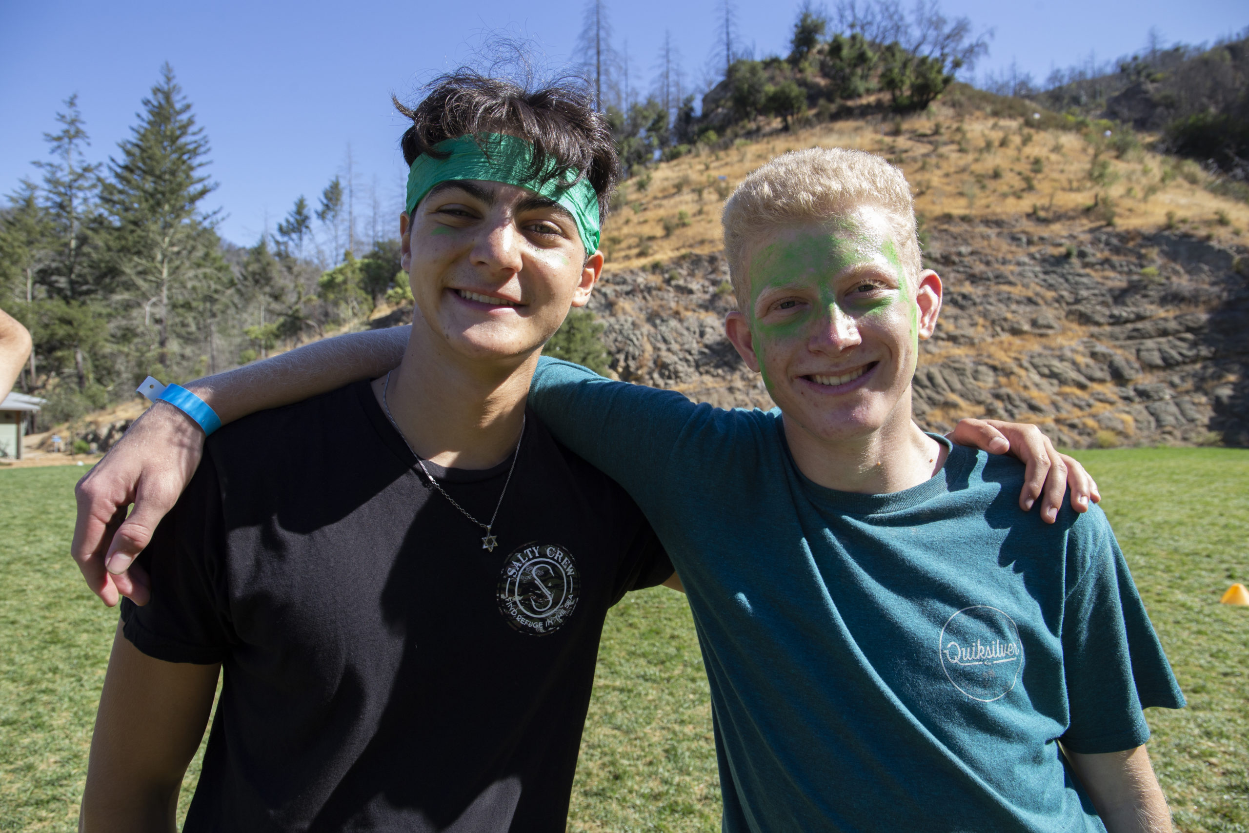 Two campers with green shirts and green face paint hugging at summer camp.